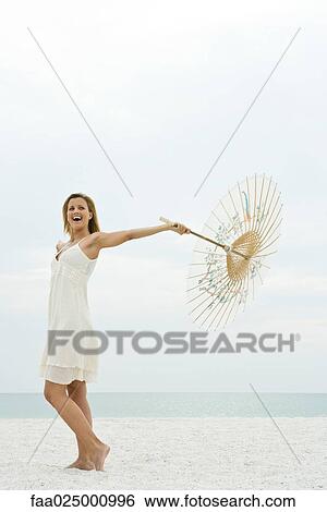 Stock Photograph - Woman holding parasol on beach, full length. Fotosearch