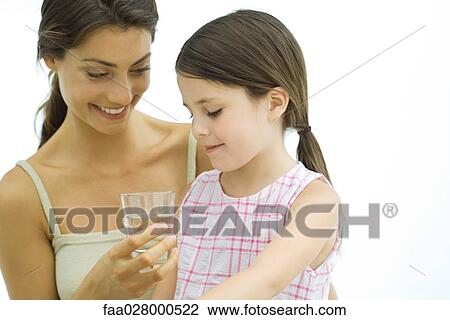 Stock Image - Woman holding up glass of water for girl. Fotosearch