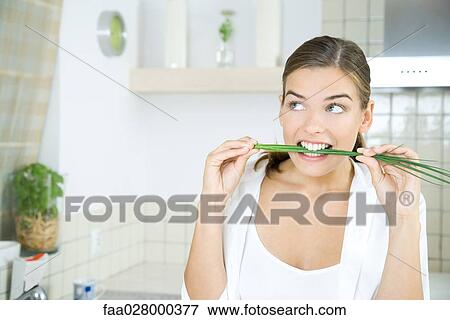 Woman in kitchen, biting into fresh chives, looking away View Large Photo Image Stock Photo - Woman in kitchen, biting into fresh chives, looking away. Fotosearch