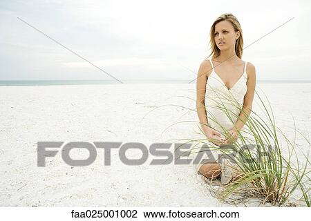 Woman kneeling on beach by dune grass, looking away, full length View Large Photo Image Stock Image - Woman kneeling on beach by dune grass, looking away, full length. Fotosearch