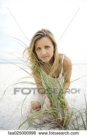 Woman kneeling on beach, looking through tall grass View Large Photo Image Stock Photo - Woman kneeling on beach, looking through tall grass. Fotosearch