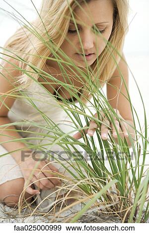 Stock Photo - Woman kneeling on beach, looking through tall grass. Fotosearch