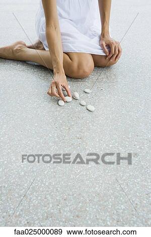 Woman kneeling on the ground arranging pebbles, cropped view View Large Photo Image Stock Photo - Woman kneeling on the ground arranging pebbles, cropped view. Fotosearch