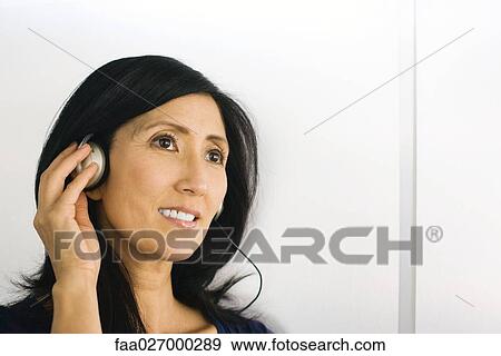 Woman listening to headphones, smiling, looking away View Large Photo Image Stock Photo - Woman listening to headphones, smiling, looking away. Fotosearch