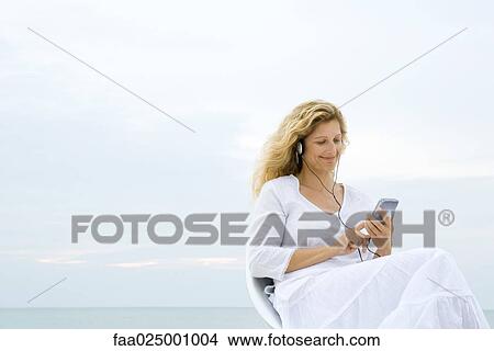 Woman listening to MP3 player, ocean horizon in background View Large Photo Image Picture - Woman listening to MP3 player, ocean horizon in background. Fotosearch