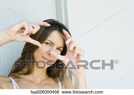 Stock Photograph - Woman looking through finger frame, smiling at camera. Fotosearch