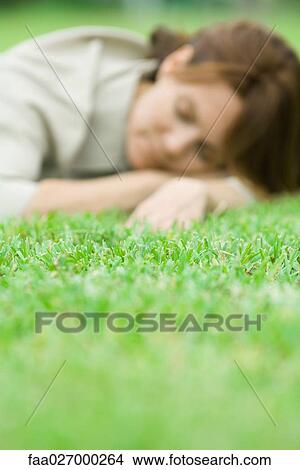 Woman lying in grass, head resting on arms, eyes closed, selective focus View Large Photo Image Picture - Woman lying in grass, head resting on arms, eyes closed, selective focus. Fotosearch