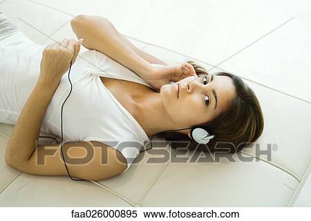 Woman lying on back, listening to headphones, looking at camera, high angle view View Large Photo Image Stock Photography - Woman lying on back, listening to headphones, looking at camera, high angle view. Fotosearch