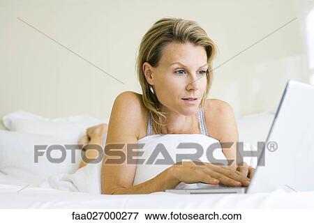 Woman lying on bed, using laptop computer, looking away View Large Photo Image Stock Photo - Woman lying on bed, using laptop computer, looking away. Fotosearch