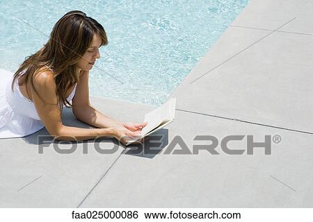 Woman lying on stomach next to pool, reading book View Large Photo Image Stock Photograph - Woman lying on stomach next to pool, reading book. Fotosearch