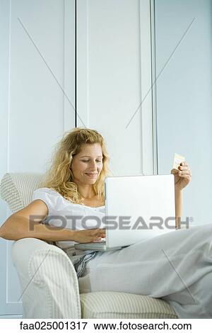 Woman making online purchase with credit card, sitting in armchair with laptop on lap View Large Photo Image Stock Photo - Woman making online purchase with credit card, sitting in armchair with laptop on lap. Fotosearch