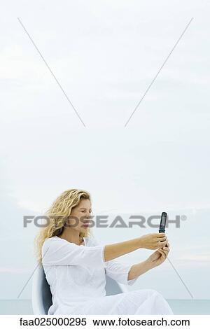 Woman photographing self with cell phone, sticking out tongue, eyes closed View Large Photo Image Stock Photography - Woman photographing self with cell phone, sticking out tongue, eyes closed. Fotosearch