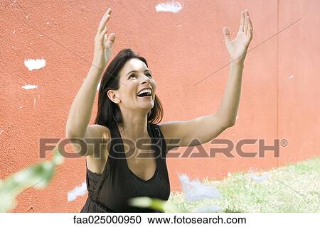 Woman raising arms, laughing, while feathers fall around her View Large Photo Image Stock Image - Woman raising arms, laughing, while feathers fall around her. Fotosearch