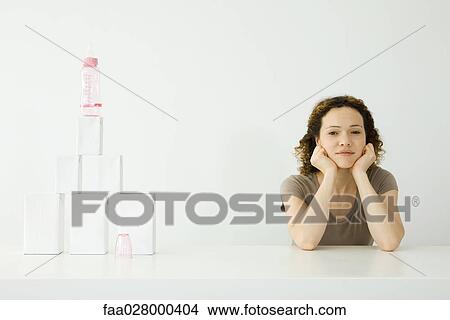 Woman sitting at table beside baby bottle and stacked milk cartons, holding head and looking at camera View Large Photo Image Picture - Woman sitting at table beside baby bottle and stacked milk cartons, holding head and looking at camera. Fotosearch