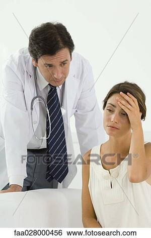 Woman sitting, holding head, doctor leaning over behind her View Large Photo Image Stock Photograph - Woman sitting, holding head, doctor leaning over behind her. Fotosearch