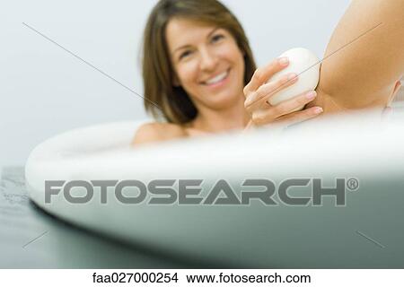 Woman sitting in bathtub, washing leg with soap, smiling View Large Photo Image Picture - Woman sitting in bathtub, washing leg with soap, smiling. Fotosearch