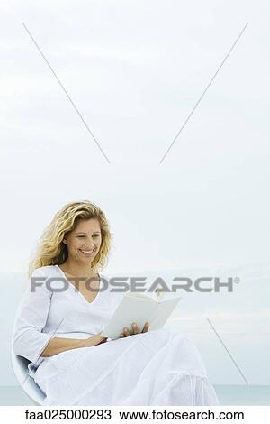 Woman sitting in chair outdoors, reading book, smiling View Large Photo Image Stock Image - Woman sitting in chair outdoors, reading book, smiling. Fotosearch