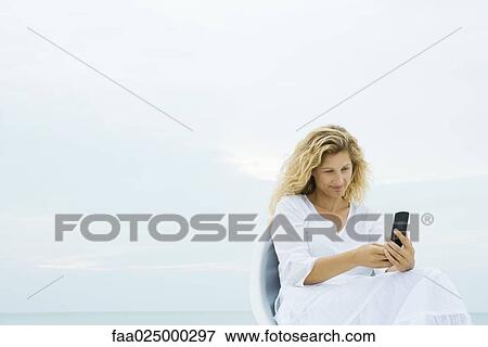 Woman sitting in chair outdoors, looking at cell phone View Large Photo Image Stock Photo - Woman sitting in chair outdoors, looking at cell phone. Fotosearch