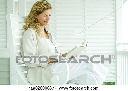 Woman sitting in rocking chair, reading book, smiling View Large Photo Image Stock Photo - Woman sitting in rocking chair, reading book, smiling. Fotosearch