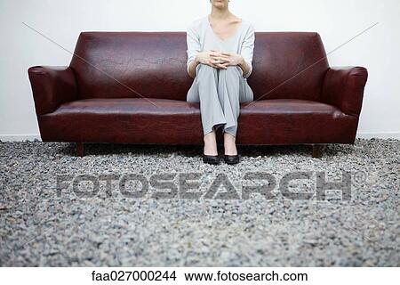 Picture - Woman sitting on couch in gravel, low angle view, cropped. Fotosearch