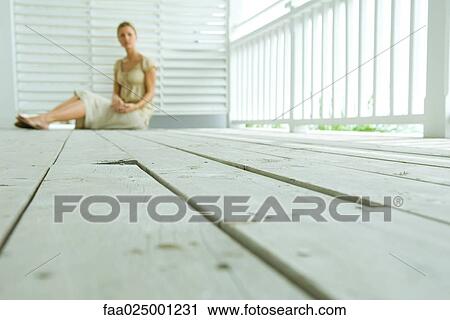 Stock Image - Woman sitting on deck, focus on wooden planks, surface level view. Fotosearch