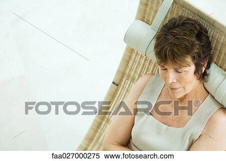Stock Photography - Woman sitting on lounge chair, eyes closed, high angle view. Fotosearch