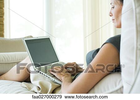 Woman sitting on sofa, using laptop computer, side view View Large Photo Image Stock Photo - Woman sitting on sofa, using laptop computer, side view. Fotosearch