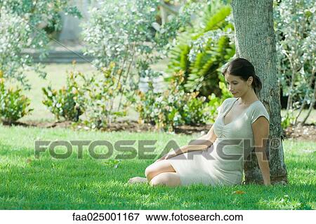 Woman sitting on the ground under tree, smiling, looking down View Large Photo Image Stock Photo - Woman sitting on the ground under tree, smiling, looking down. Fotosearch