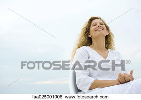 Woman sitting with eyes closed and head back, smiling, sky in background, low angle view View Large Photo Image Stock Photograph - Woman sitting with eyes closed and head back, smiling, sky in background, low angle view. Fotosearch