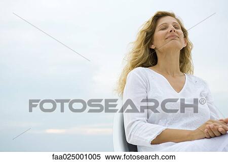 Woman sitting with eyes closed, smiling, sky in background, low angle view View Large Photo Image Stock Photography - Woman sitting with eyes closed, smiling, sky in background, low angle view. Fotosearch
