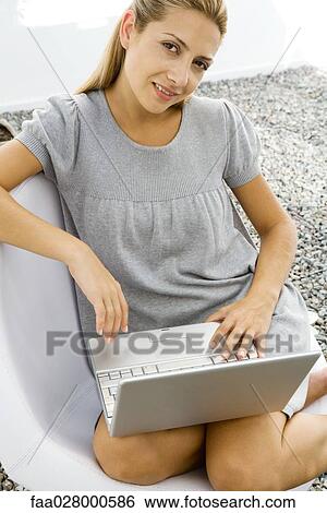 Stock Photograph - Woman sitting with laptop on lap, smiling at camera. Fotosearch