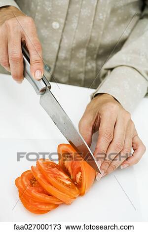Stock Image - Woman slicing tomato with knife, cropped view. Fotosearch