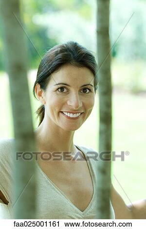 Woman smiling at camera through trees, portrait View Large Photo Image Stock Image - Woman smiling at camera through trees, portrait. Fotosearch