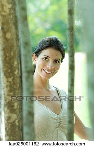 Woman smiling at camera through trees, portrait View Large Photo Image Stock Image - Woman smiling at camera through trees, portrait. Fotosearch