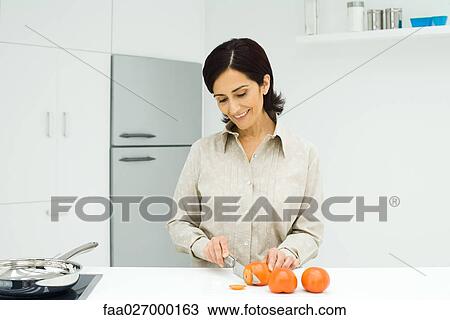 Woman standing at kitchen counter, slicing tomatoes with knife View Large Photo Image Stock Image - Woman standing at kitchen counter, slicing tomatoes with knife. Fotosearch