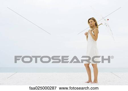 Woman standing at the beach holding parasol, looking away View Large Photo Image Stock Photo - Woman standing at the beach holding parasol, looking away. Fotosearch