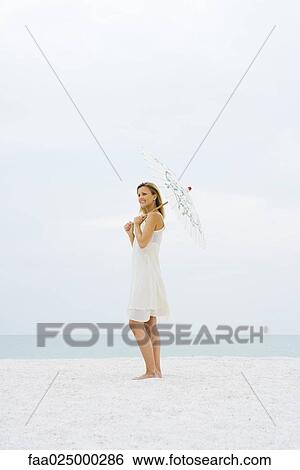 Woman standing at the beach holding parasol, looking away View Large Photo Image Stock Photograph - Woman standing at the beach holding parasol, looking away. Fotosearch