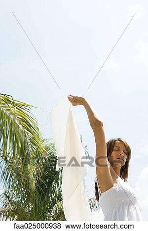 Woman standing in sun in tropical setting, holding up wrap, eyes closed, low angle view View Large Photo Image Stock Photo - Woman standing in sun in tropical setting, holding up wrap, eyes closed, low angle view. Fotosearch