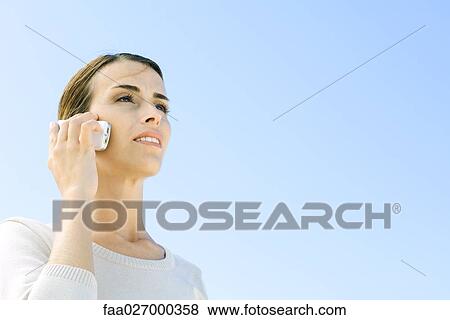 Woman using cell phone outdoors, looking away, low angle view View Large Photo Image Stock Photo - Woman using cell phone outdoors, looking away, low angle view. Fotosearch