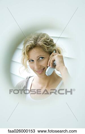 Woman using cell phone, smiling, viewed through hole View Large Photo Image Stock Image - Woman using cell phone, smiling, viewed through hole. Fotosearch