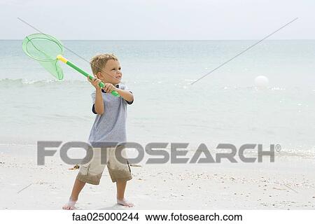 Picture - Young boy at the beach, holding up net to catch ball. Fotosearch