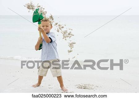 Young boy at the beach holding up shovel, throwing sand, eyes closed View Large Photo Image Stock Image - Young boy at the beach holding up shovel, throwing sand, eyes closed. Fotosearch