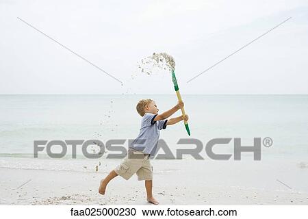 Young boy at the beach, holding up shovel and throwing sand, side view View Large Photo Image Stock Image - Young boy at the beach, holding up shovel and throwing sand, side view. Fotosearch