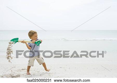 Young boy at the beach, holding up shovel and spilling sand View Large Photo Image Stock Image - Young boy at the beach, holding up shovel and spilling sand. Fotosearch