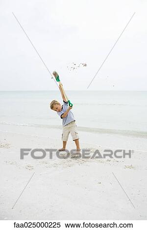 Stock Photography - Young boy at the beach holding up shovel, throwing sand. Fotosearch