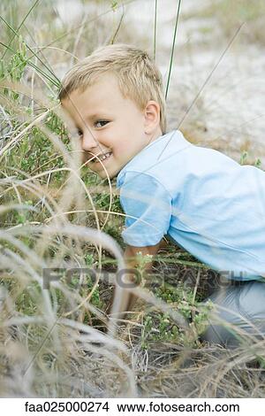 Young boy crouching in tall grass, looking over shoulder at camera View Large Photo Image Picture - Young boy crouching in tall grass, looking over shoulder at camera. Fotosearch