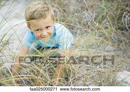 Young boy crouching in tall grass, looking away, smiling View Large Photo Image Stock Image - Young boy crouching in tall grass, looking away, smiling. Fotosearch