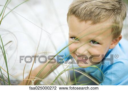 Young boy crouching in tall grass, smiling at camera View Large Photo Image Stock Image - Young boy crouching in tall grass, smiling at camera. Fotosearch