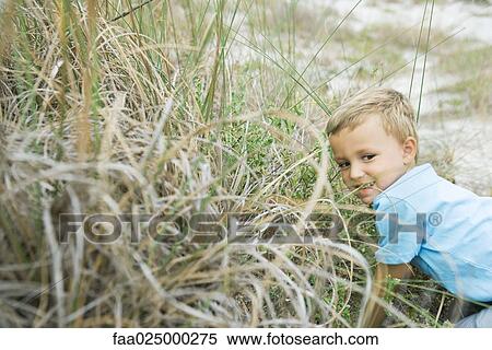 Young boy crouching in tall grass, looking away View Large Photo Image Stock Photography - Young boy crouching in tall grass, looking away. Fotosearch