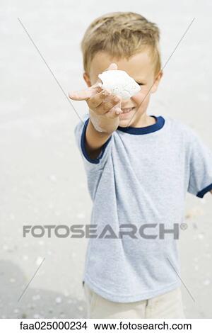 Young boy holding up seashell, focus on foreground View Large Photo Image Picture - Young boy holding up seashell, focus on foreground. Fotosearch